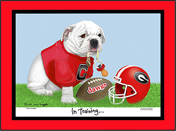 Georgia baby bulldog sitting in the grass, wearing a red tee shirt with Georgia logo and holding a doggie pacifier in his mouth. There is a football and helmet next to him. In Training is printed under the graphic